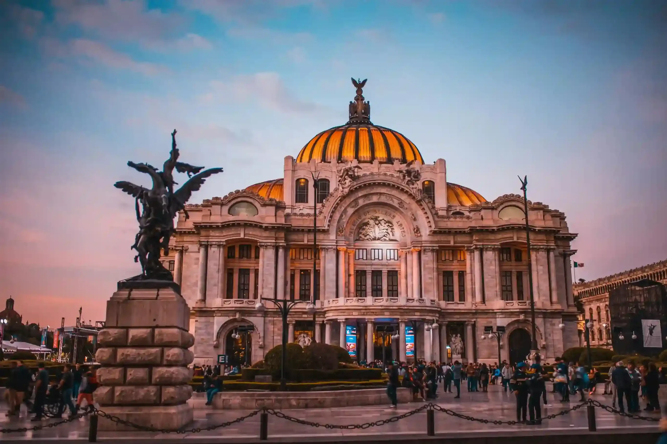 Palacio de Bellas Artes en Ciudad de México al atardecer, con cielo rosado y visitantes en la explanada