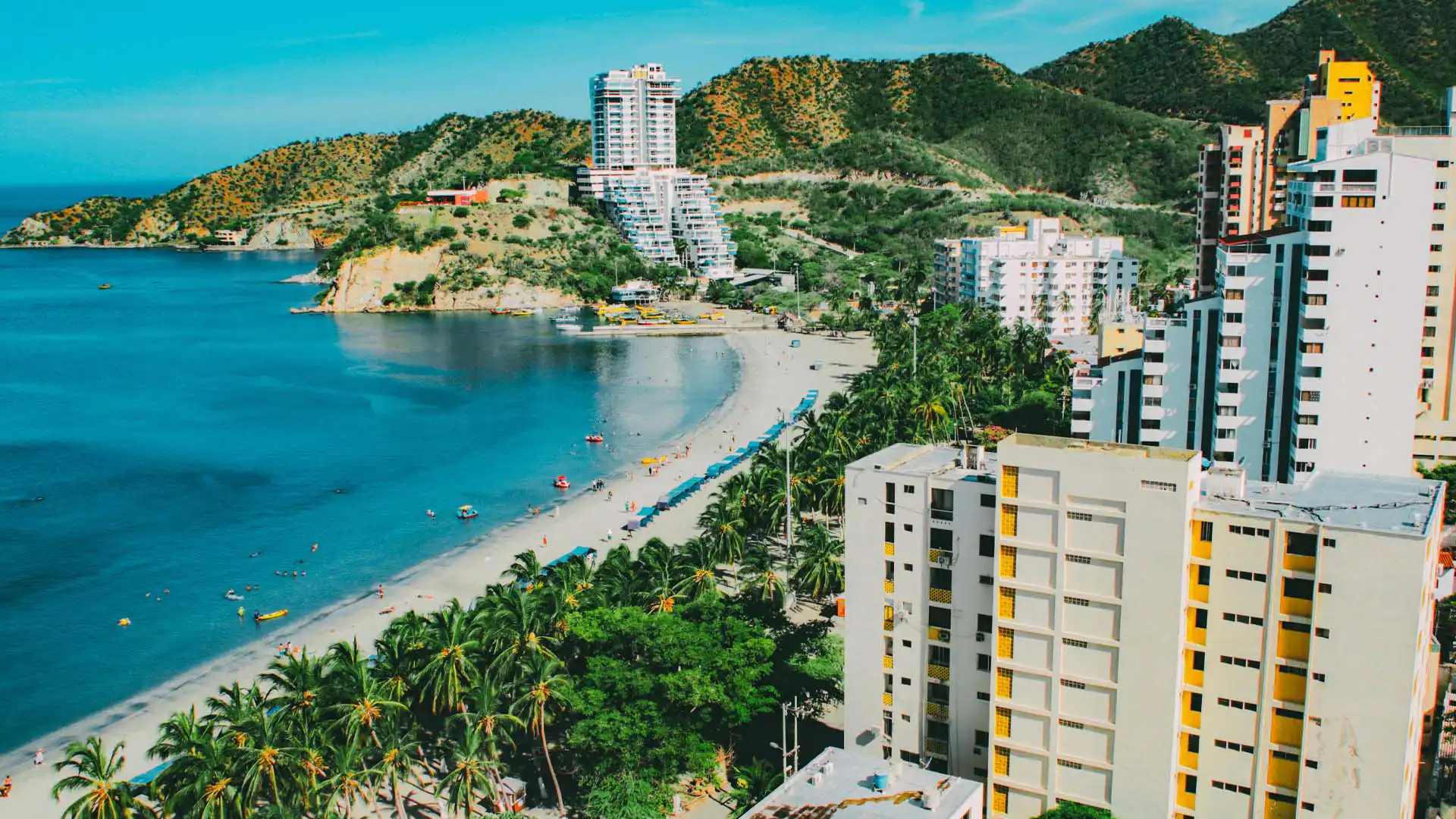Vista aérea de playa tropical con edificios modernos, palmeras y mar azul en Colombia
