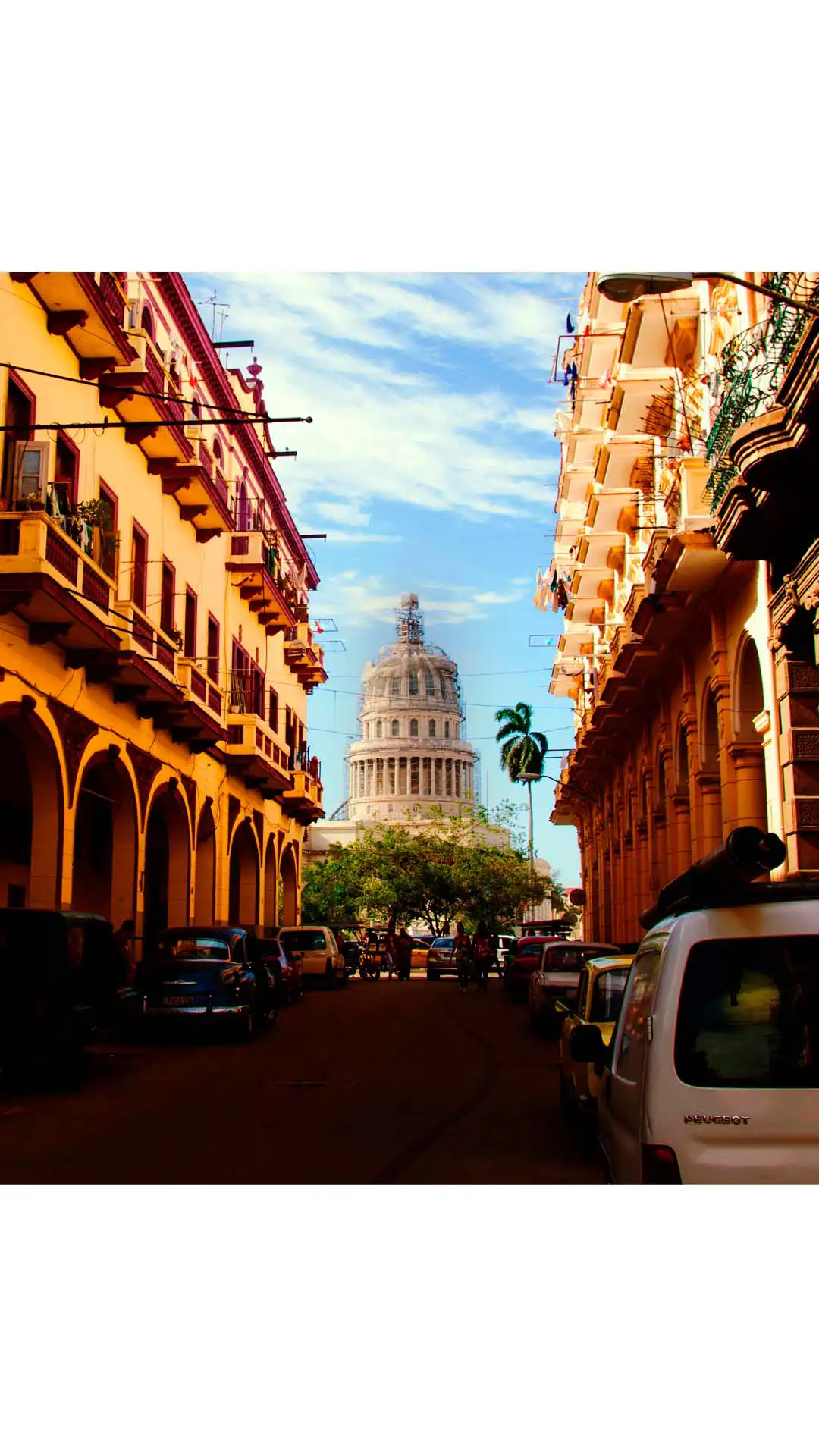 Vista del Capitolio de La Habana desde una calle con edificios coloniales y autos antiguos en Cuba