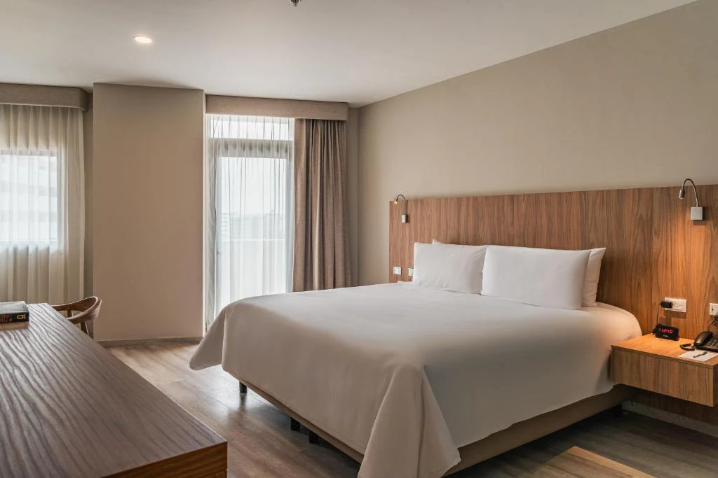 Habitación moderna con cama king size, decoración minimalista y ventanal con vista a la piscina en hotel Wyndham México.