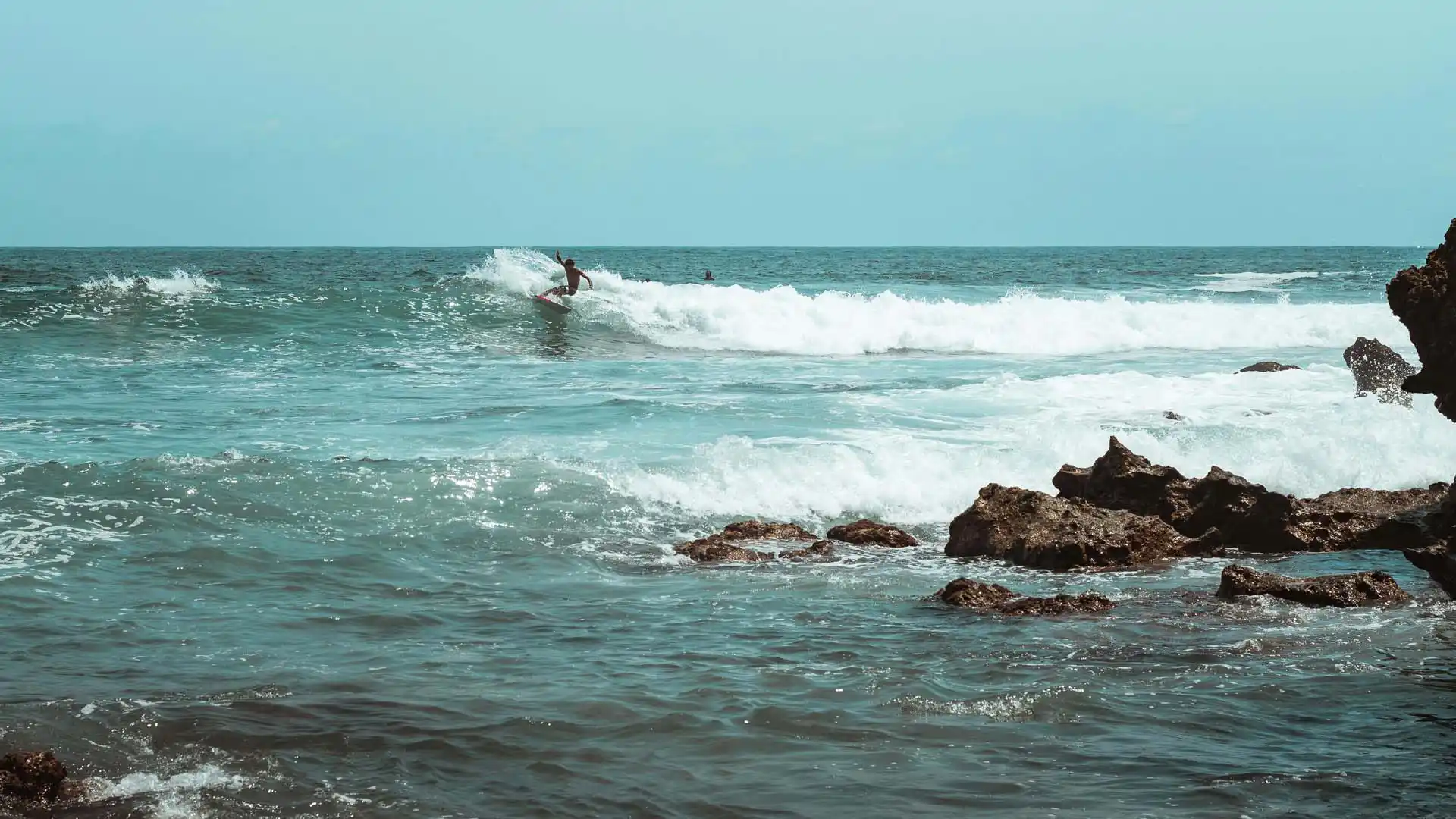 Surfista en las olas de Puerto Escondido, Oaxaca, rodeado de mar azul y formaciones rocosas