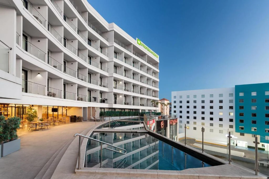 Vista exterior del Hotel Wyndham México con piscina iluminada al atardecer y terrazas modernas.