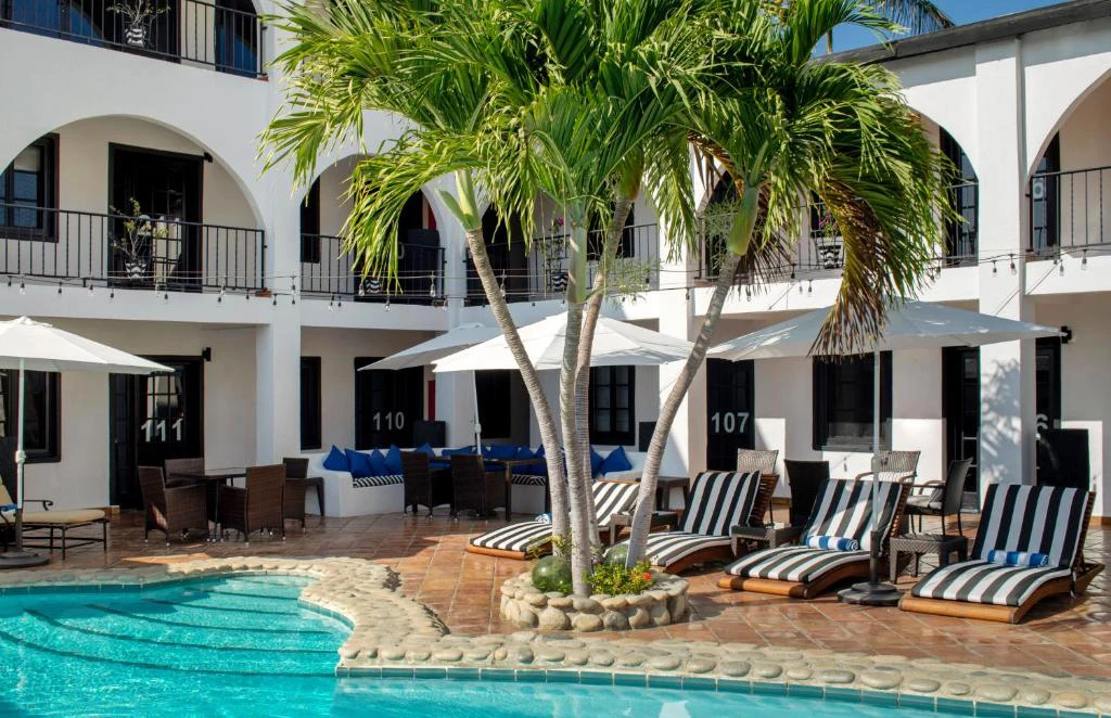 Piscina rodeada de palmeras y camastros con vista a balcones del Hotel La Marina Inn en Los Cabos, México.